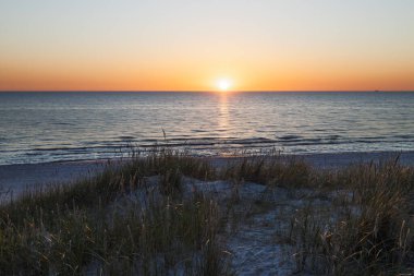 Sakin dalgalar, kumlu kıyılar ve kumlu otlarla Baltık Denizi 'nin üzerinde ılık gün batımı.