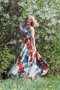 Eğlenceli bir kız dans ediyor ve eğleniyor. Bahar günü. Sağlıklı bir insanın enerjisi, açık havada duygusal dinlenme. Çiçekli uzun elbiseli kız. beyaz kiraz çiçekleri