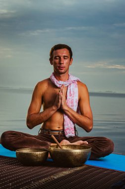 Pantolon giymiş bir adam. Okyanusun üzerindeki günbatımının arka planında oturuyordu. Ruhsal adam, ezoterizm eğitimi, yoga egzersizleri. Bakır Tibet 