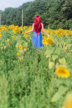 Özgür kız sahada yürüyor. Huzur ve sükunet insanın neşesini doldurur. Kırmızı peruk, uzun mavi etek