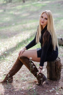 Eğlenceli bir kız dans ediyor ve eğleniyor. Bahar günü. Sağlıklı bir insanın enerjisi, açık havada duygusal dinlenme. Sarışın ormandaki bir kütükte oturuyor.