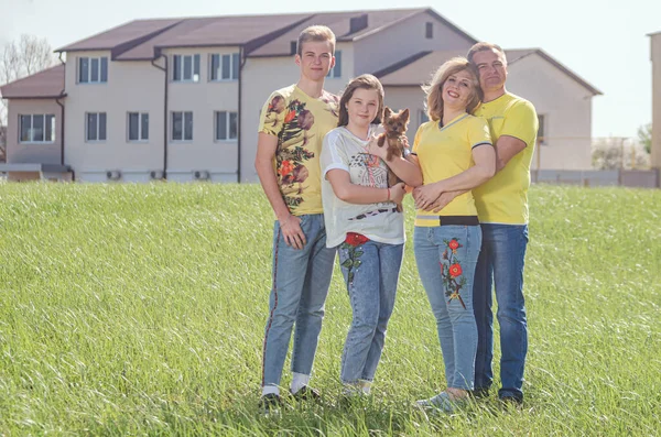 the seed stands against the background of the cottage.  father, mother, daughter, son and little dog.  good parents, parental home.  summer, warm day, green lawn.