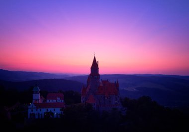 Pembe ve mor akşam gökyüzüne karşı pitoresk yayla manzara romantik peri masalı kale bir siluet üzerinde havadan görünümü. Birçok kuleleri ile Castle Bouzov, Moravya manzara, Çek Cumhuriyeti.