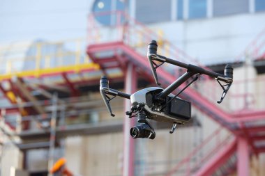 Yükseltilmiş iniş takımları ve bulanık endüstriyel inşaata karşı güçlü kamera ile siyah quadcopter hovering. Endüstride havadan ulaşılması zor nesnelerin görsel denetimi. Yan görünüm.