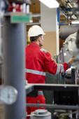 Energiewirtschaft. Ein Techniker in roten Overalls und weißem Helm überprüft die Heizparameter. Heizungstechnologie zur Wasserverteilung. Servicearbeiten in der Energiewirtschaft.