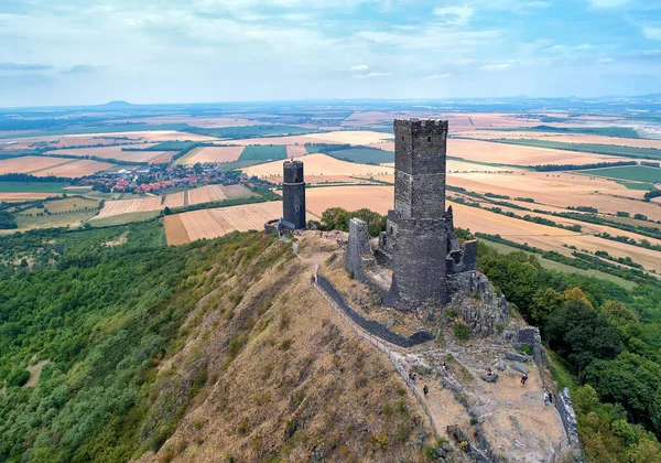 Aerial, distant  view of two stone towers,  ruins of medieval castle Hazmburk, Hasenburg built on top of the mountain peak, surrounded by agriculture czech landscape. Tourist attraction, castles of western Bohemia, Czech republic.