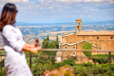 Tuscan kırsalına karşı elinde gümüş şarap kadehi tutan beyaz elbiseli bir kadının bulanık silueti. İtalya 'da yaz tatili.