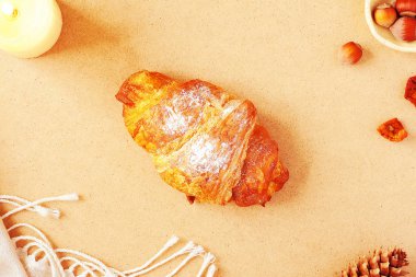 Rahat sonbahar düzeni - kruvasan ile fındık, köknar koni, mum ve eşarp pastel kremsi ahşap arka plan üzerinde. Üstten görünüm