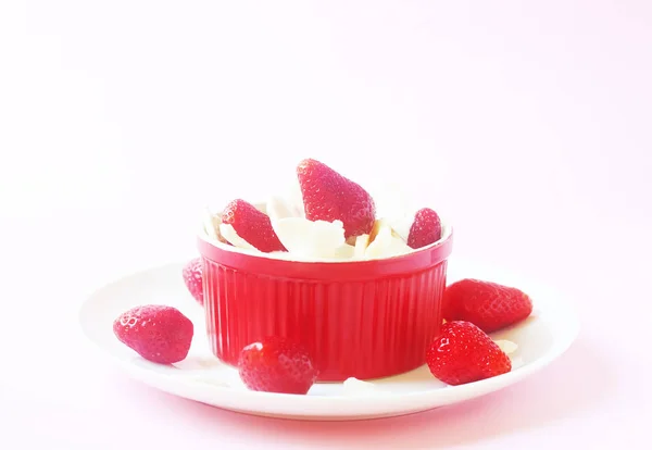 Healthy raw vegan dessert - banana and strawberry with coconut cream and coconut chips on pink background