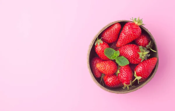Un tazón de fresas frescas orgánicas maduras con menta sobre fondo rosa, vista superior. Concepto de alimentación saludable, espacio de copia —  Fotos de Stock