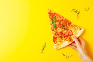 Bir dilim pizza tutan kadın Margherita, sarı arka planda salam, düz döşeme, kopyalama alanı
