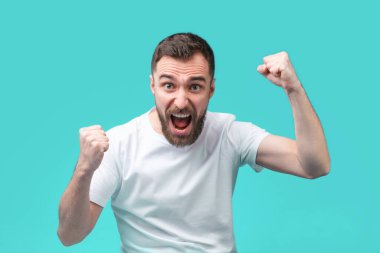 Genç sakallı hippi erkek bahisçinin internet sitesinde bahis oynadıktan sonra para kazanmaktan mutlu oluyor. Şanslı futbol taraftarı en sevdiği takımın zaferini kutluyor. Yumruklarını sıkıyor..