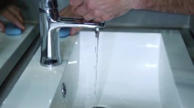 Genç bir adam evdeki lavaboda ellerini yıkıyor, umumi bir yerde, el bakımı, el dezenfeksiyonu. Yakın plan, yaşam tarzı.