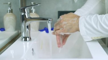 Ellerindeki sabunları durula, ellerini temiz tut, bir insan ellerini muslukta suyla yıkar, böylece koronavirüs bulaşmaz, yakın plan.