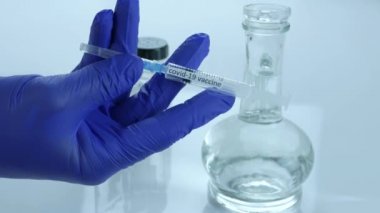 Coronavirus aşısı kelimelerini içeren bir şırınga, bir tıp çalışanı, covid-19 salgınına karşı aşıyı bir laboratuarda, yakın planda gösteriyor.
