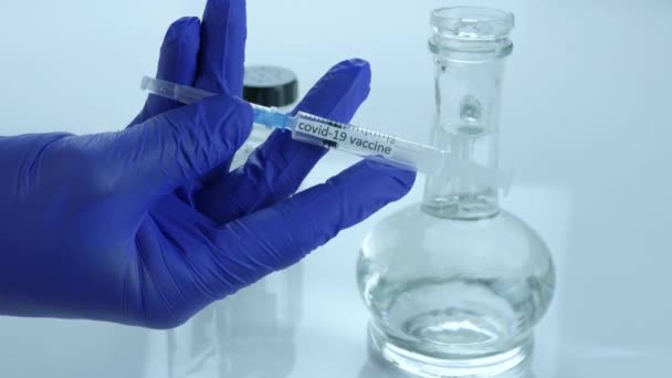 コロナウイルスワクチンという言葉を持つ注射器は 医療従事者は 研究室 クローズアップでのCovid 19パンデミックに対するワクチンを示しています — ストック動画