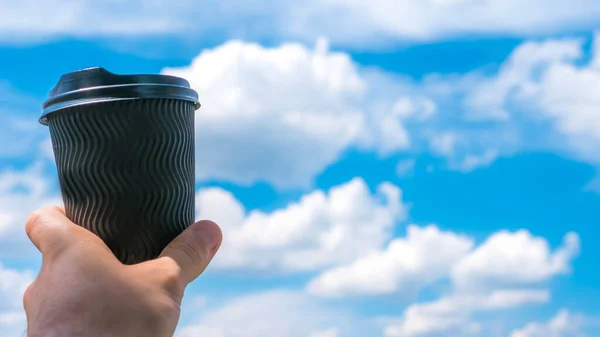 A glass of coffee on a background of the sky,a guy,a man holding coffee in his hand,close-up. Beautiful clouds and clouds,summer mood with espresso