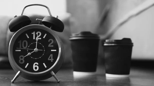 Two glasses of cappuccino and a retro clock with an alarm clock,aromatic morning coffee in the apartment,Americano in cups,the arrows are at 8 am,close-up.Black and white picture.