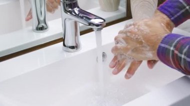 Bir adam ellerini sabunla yıkıyor, musluğun altında suyla, yakından, koronavirüs enfeksiyonundan okuyor.