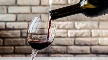 Duvarın arka planında bir bardağa kırmızı şarap dökmek. Yakın plan.