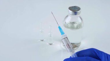 İlaç şırınganın iğnesinden aşağı akıyor, kovid 19 'a karşı aşı, viral hastalık için ilaç, doktorun eldiveni içindeki eli....