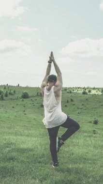 Doğada bir tarlada el kaldırmış genç bir adam, yoga yapıyor, çayırda yalnız bir adam, genç bir adam özgürlükle seviniyor..