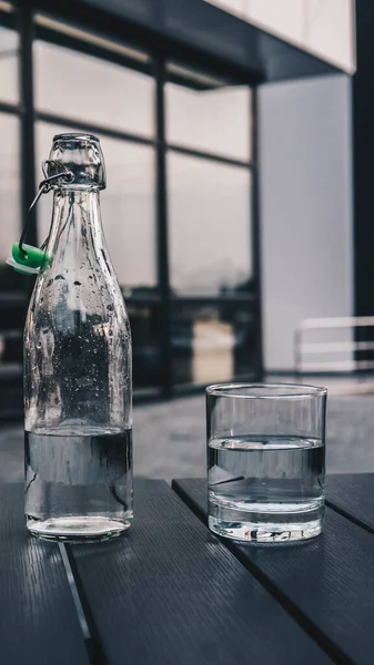 Drinking water in a glass and a glass bottle on a wooden table on the street close-up.Mineral water
