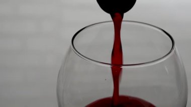 Beyaz tuğla bir duvarın arka planına karşı şişeden bardağa şarap dökmek. Bardakta kırmızı şarap yakın plan.