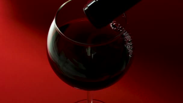 Piros bort öntsön egy üvegből egy pohárba, vörös alapon. Egy pohár vörösbor közelkép.