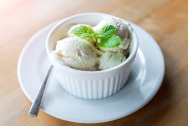 Süt vanila dondurmalar sabah sıcak aydınlatma ile beyaz fincan nane yaprağı ile.