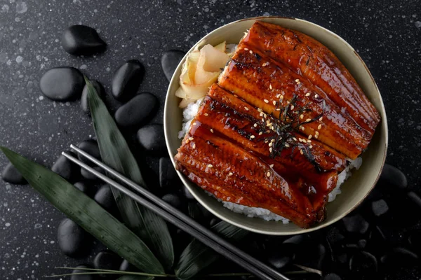Japanese grilled eel with sweet sauce on rice cup or unagi kabayaki in Japanese menu name photo with indoor lighting.