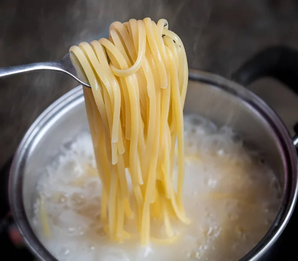 Yellow noodles or spaghetti cooking in boiling water pot.