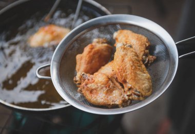 Kızarmış tuzlu tavuk kanadı, demir tavada pişirme yağı ve kapalı alanda hafif ışıklandırma..