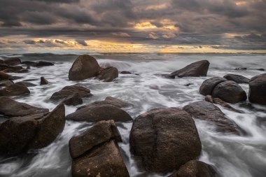 Gün batımında sert dalgalar ve kara yağmurlar ile denizdeki kayalar gökyüzünü bulutlandırır..