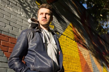 Mavi kot pantolon ve ceket giyiyor ve renkli tuğla duvar arka plan üzerinde duran bir çekici sarışın genç.