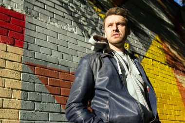 Mavi kot pantolon ve ceket giyiyor ve renkli tuğla duvar arka plan üzerinde duran bir çekici sarışın genç.