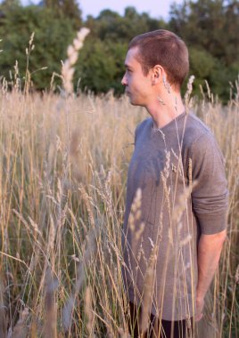 Uzun çimenlerin üzerinde orman arka plan ayakta genç çekici ince biri. Parkta genç öğrenci yan görünüm portre.