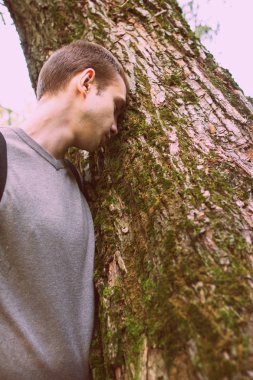 Ağaç tarafından ayakta üzgün bir genç adam. Yan görünümü bir genç çekici adam portresi.