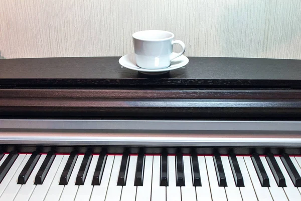 一个白色的茶托和一杯茶在粗壮的打开的钢琴 — 图库照片