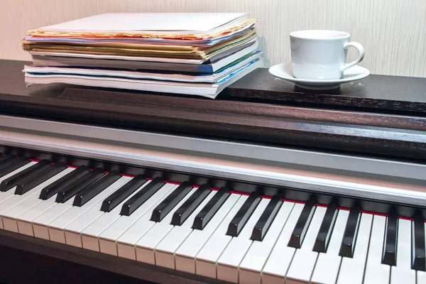 一叠乐谱和一个白色的茶托和一杯茶在勇敢的打开的钢琴上 — 图库照片