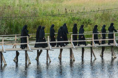 2009.08.29, Vladimir, Russia. nuns in black clothes cross the bridge and going to the monastery. clipart