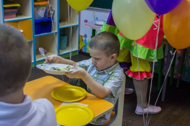 2019.01.22, Moskova, Rusya. Şenlik masasının yanında oturan ve tabağı tutan bir çocuk. Bahçede küçük bir çocuğun doğum günü kutlu olsun.