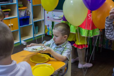 2019.01.22, Moskova, Rusya. Şenlik masasının yanında oturan ve tabağı tutan bir çocuk. Bahçede küçük bir çocuğun doğum günü kutlu olsun.