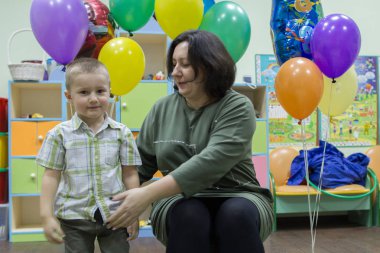 2019.01.22, Moskova, Rusya. Genç kadın ve onun küçük oğlu renkli balonlar arka plan üzerinde sandalyede oturan. 