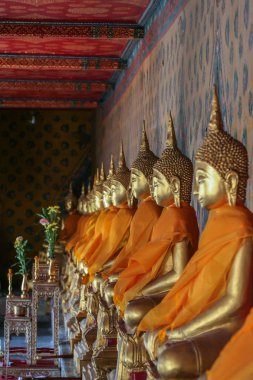 2011.04.30, Bangkok, Tayland. Turuncu bezle sarılmış duvar boyunca oturan altın Buda heykelleri bir satır sağ yan görünümü. Wat topraklarında heykeller.