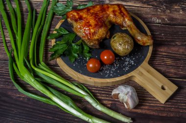 Izgara tavuk, patates, domates, salata, yeşil soğan ve taş plaka üzerinde tuz. Ahşap arka planda ızgara gıda. 