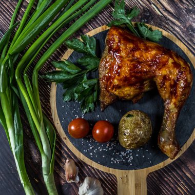 Izgara tavuk, patates, domates, salata, yeşil soğan ve taş plaka üzerinde tuz. Ahşap arka planda ızgara gıda. 