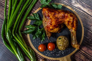 Izgara tavuk, patates, domates, salata, yeşil soğan ve taş plaka üzerinde tuz. Ahşap arka planda ızgara gıda. 