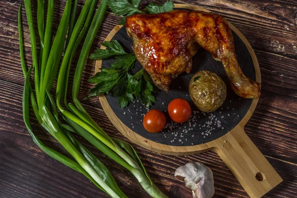 Izgara tavuk, patates, domates, salata, yeşil soğan ve taş plaka üzerinde tuz. Ahşap arka planda ızgara gıda. 