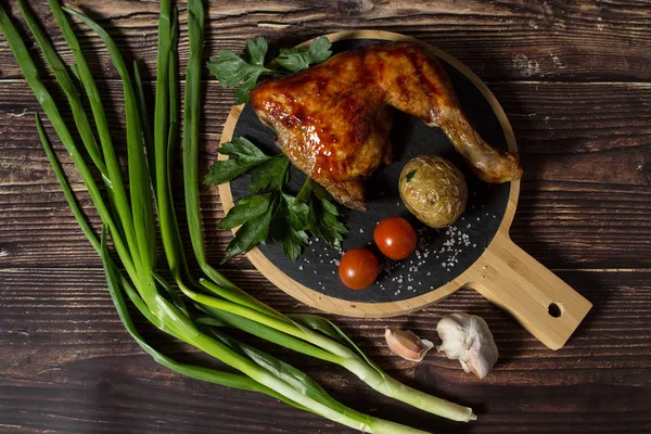 Izgara tavuk, patates, domates, salata, yeşil soğan ve taş plaka üzerinde tuz. Ahşap arka planda ızgara gıda. 